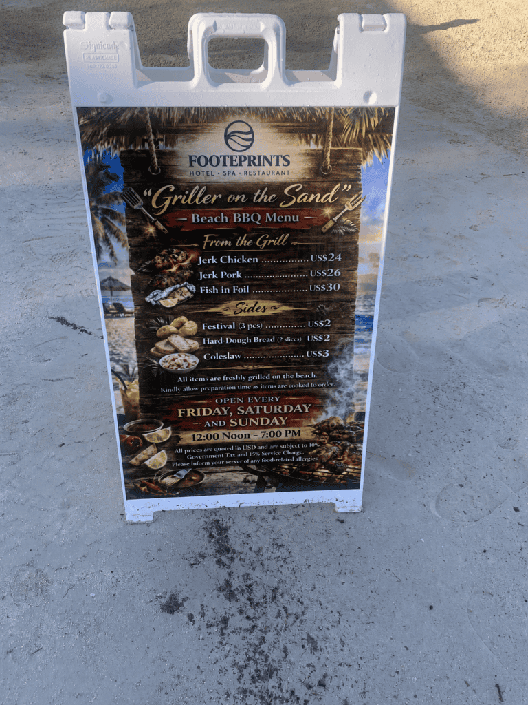 Footprints Restaurant beach BBQ menu sign in Negril Jamaica showing grilled meats, fish, sides, and opening hours.