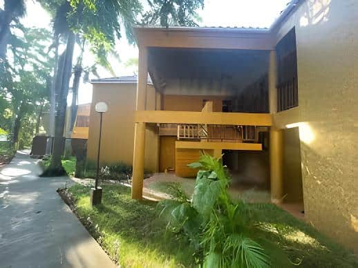Two-story tan building with yellow balconies, lush greenery, and side pathway in Negril Jamaica.