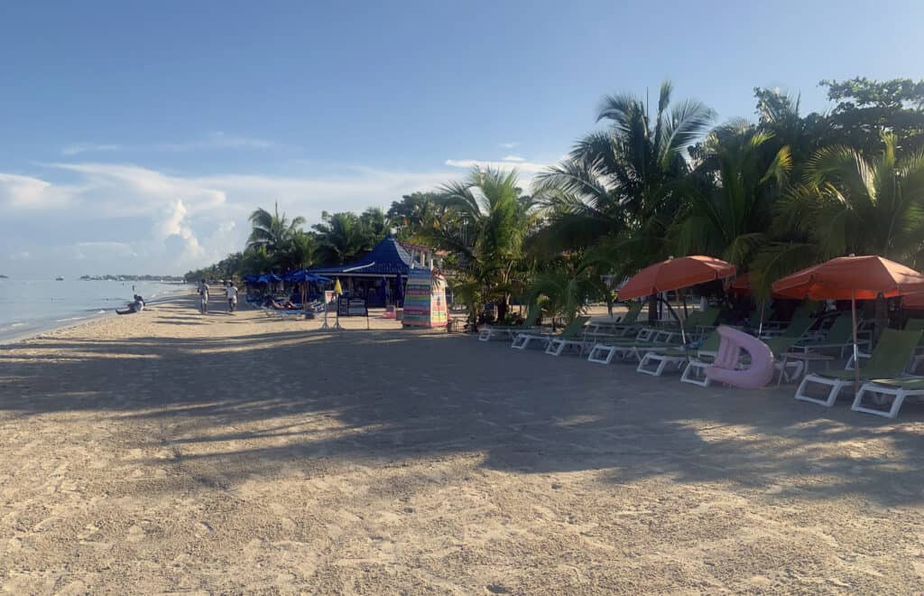 Negril Jamaica beach with palm trees, empty lounge chairs, colorful umbrellas, and a small beach hut.