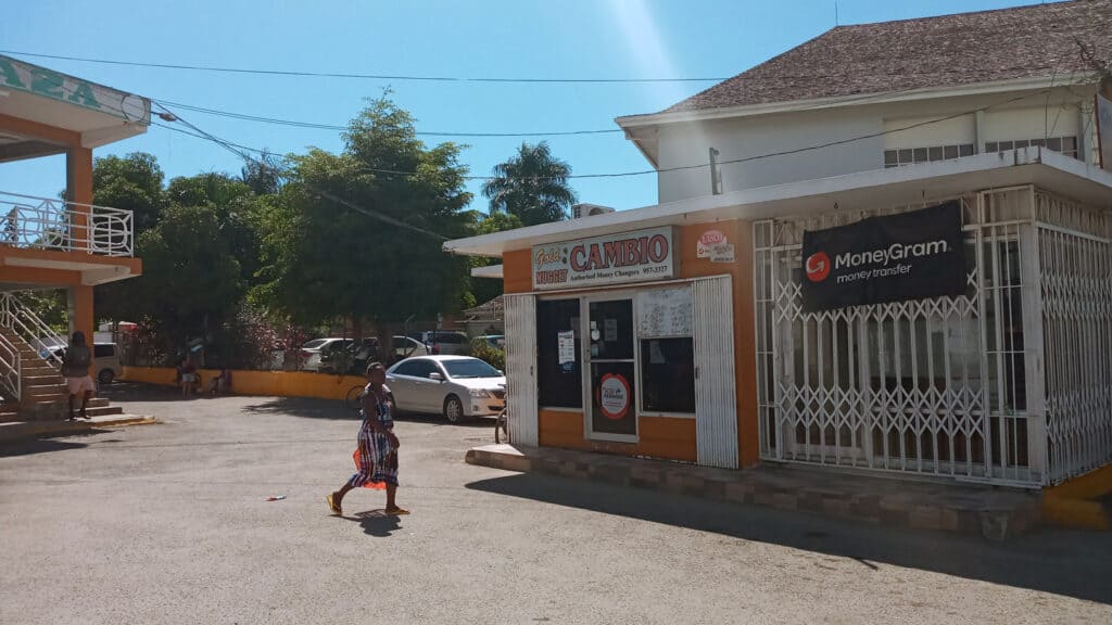 Woman walking by a currency exchange and MoneyGram office in Negril Jamaica on a sunny day.