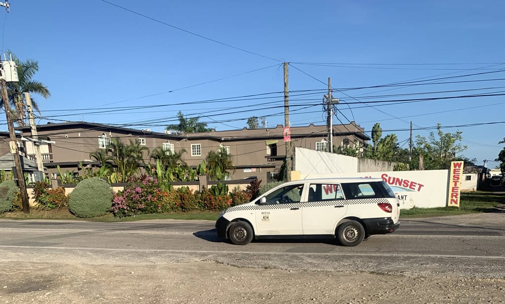White taxi passes Sunset hotel and restaurant on a sunny day in Negril, Jamaica.