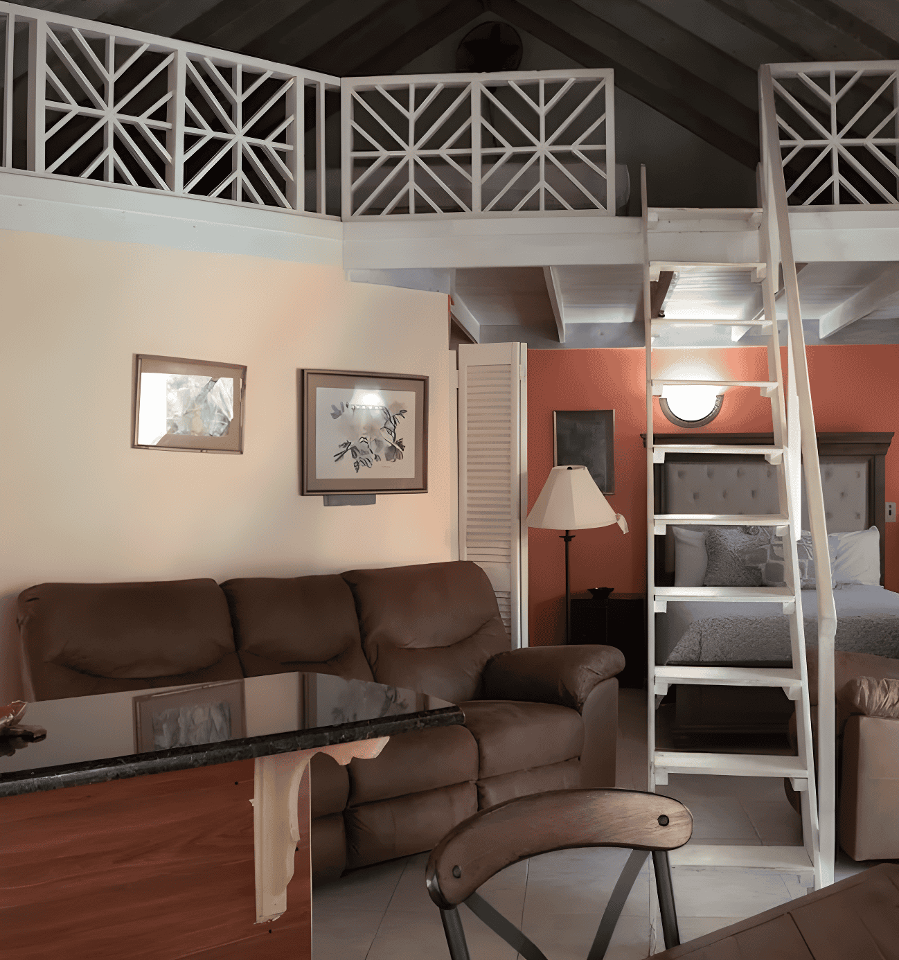 Cozy loft-style room in Negril Jamaica with sofa, bed, upper loft ladder, and warm, inviting decor.