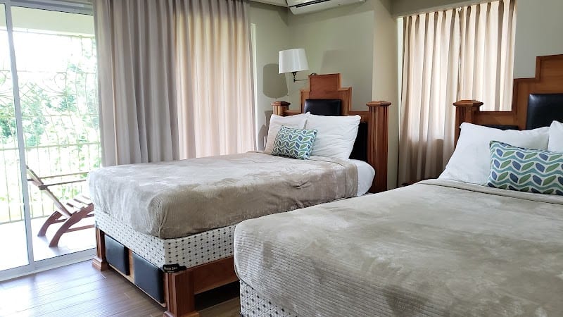 Bright Negril Jamaica hotel room with two double beds, beige curtains, and a sliding glass door opening to a balcony.