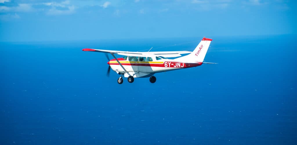 TimAir Single-engine airplane flying over the deep blue ocean under clear skies near Negril Jamaica.