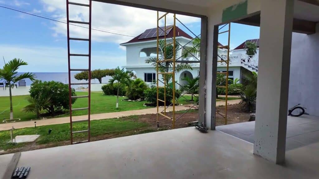 Negril Jamaica construction site view with garden, palm trees, and white seaside house overlooking the Caribbean Sea.