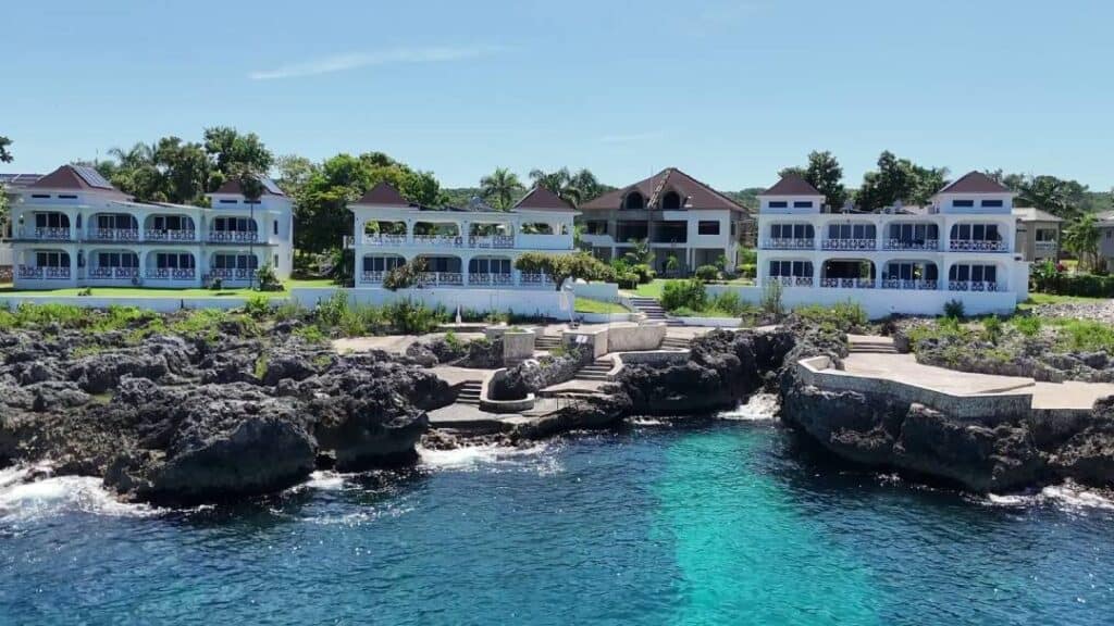 Negril Jamaica seaside villas with balconies overlooking rocky cliffs and turquoise ocean under a sunny blue sky.