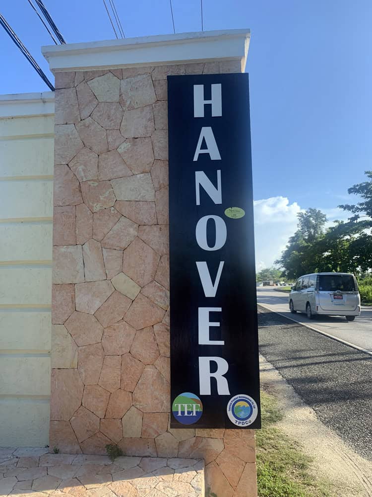 HANOVER black vertical sign on stone pillar by roadside in Negril Jamaica, van passing nearby.