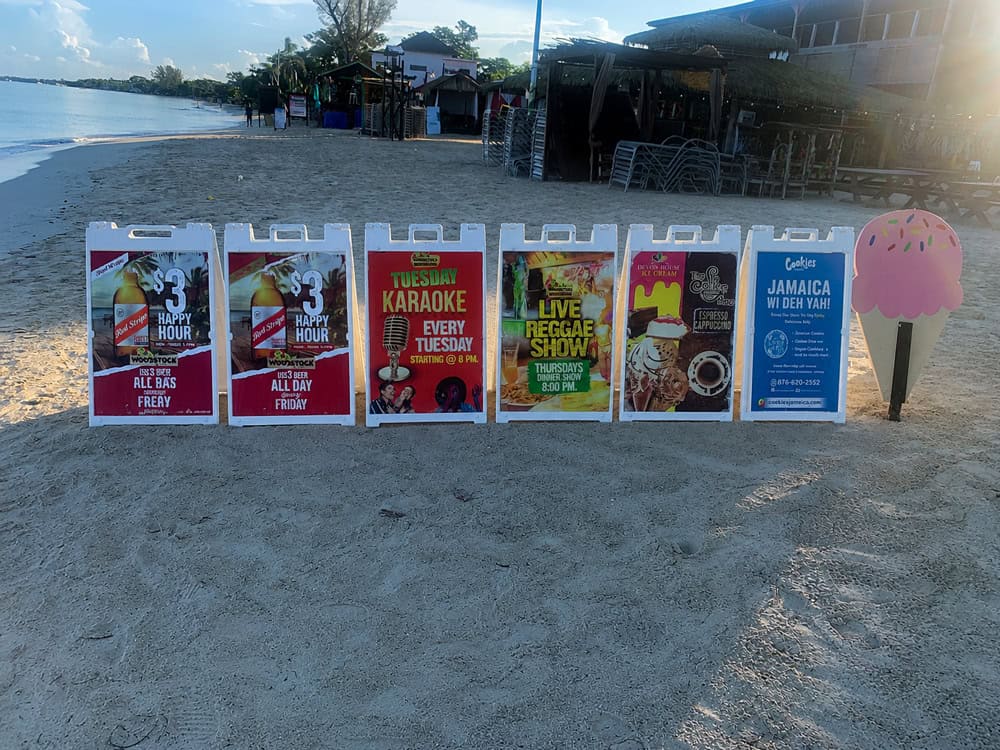 Colorful event signs and an ice cream cone cutout on Negril Jamaica’s sandy beach near the ocean.