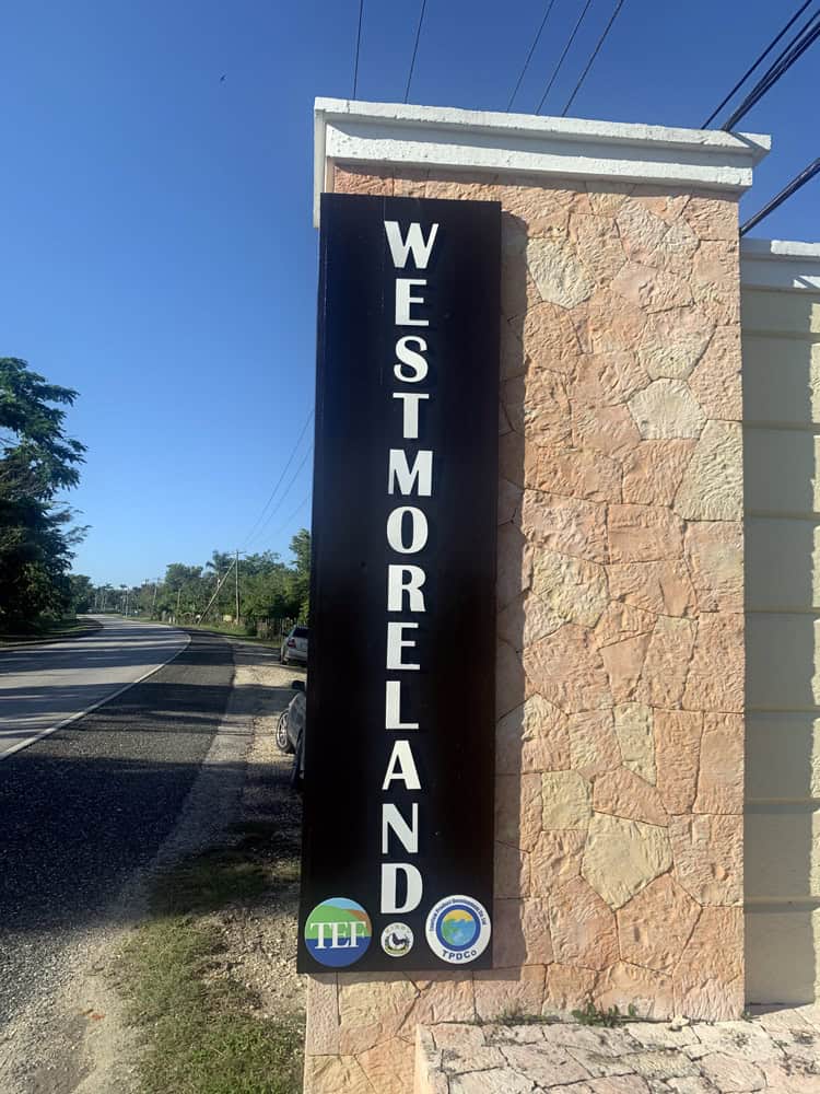 WESTMORELAND sign in white letters on a black background atop a stone wall by the roadside in Negril, Jamaica.