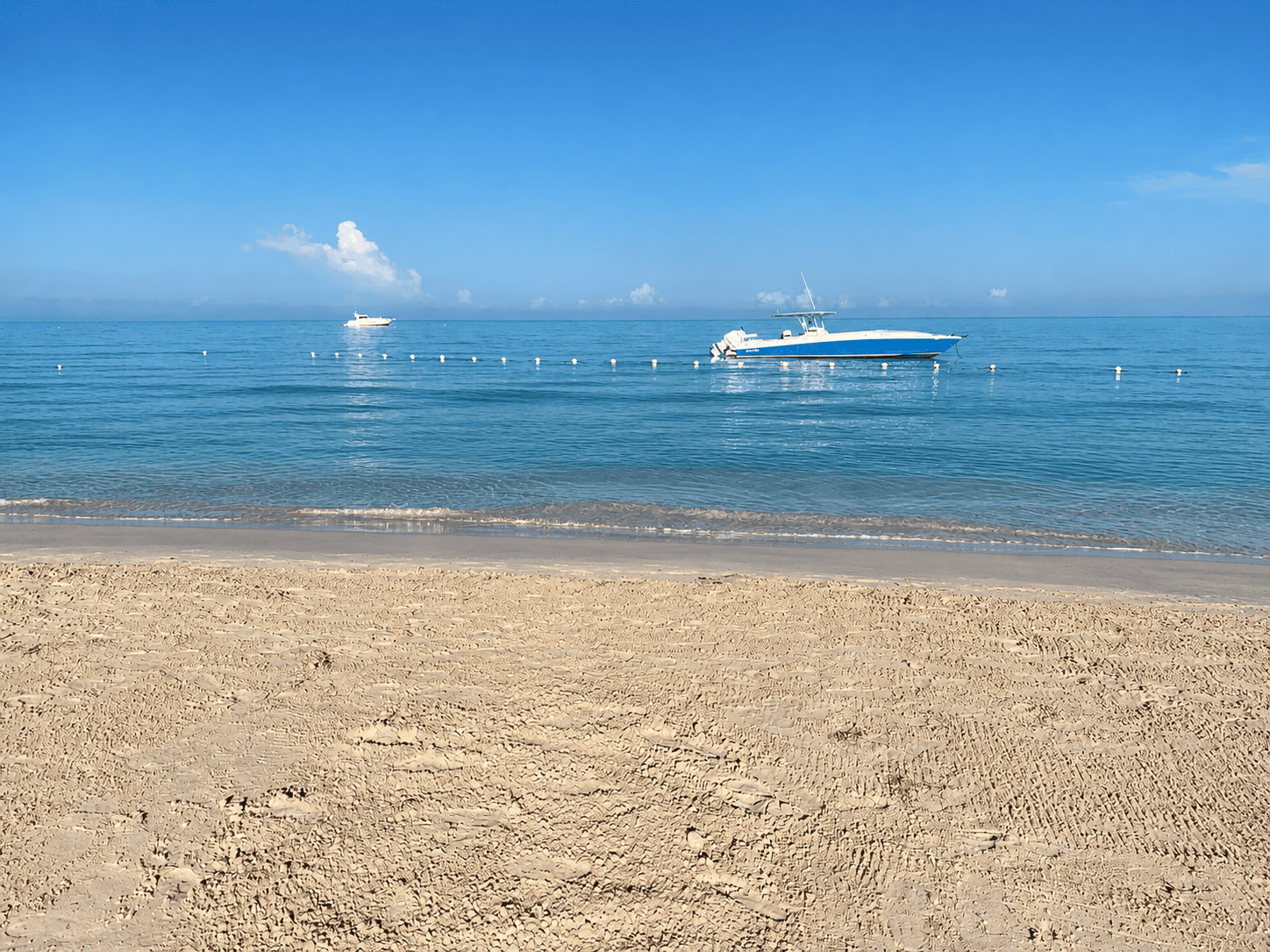 Boats anchored in calm turquoise water off a sandy beach in Negril, Jamaica.